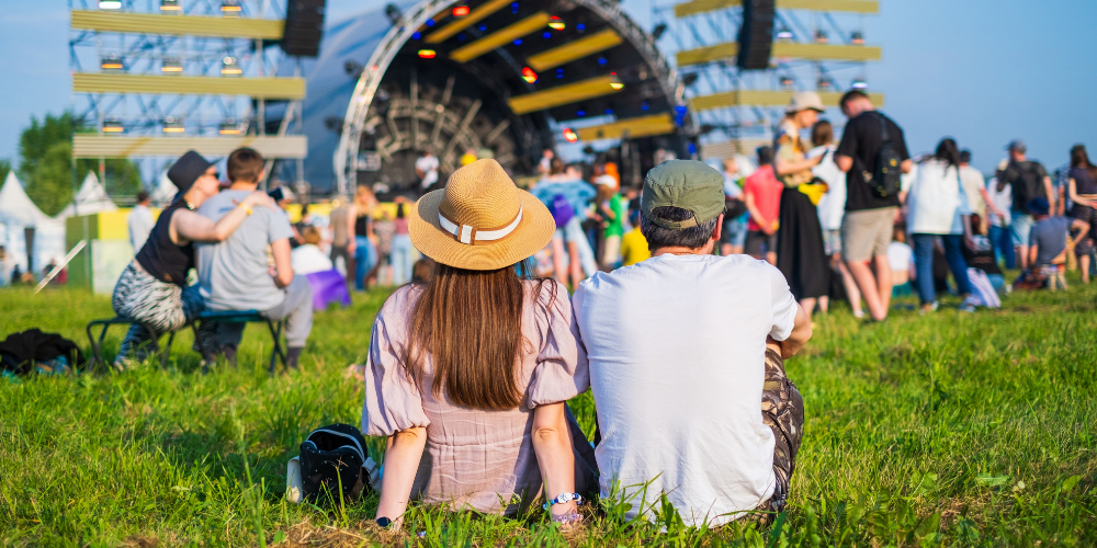 Couple sits with their back to the camera during music festival on summer day.