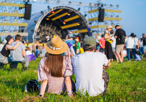 Couple sits with their back to the camera during music festival on summer day.