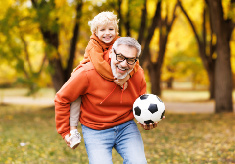 Grandfather playing soccer outdoors with his young grandson.