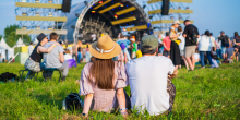 Couple sits with their back to the camera during music festival on summer day.